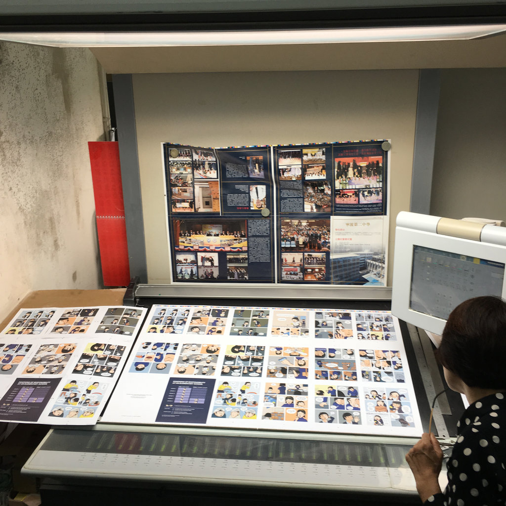 Photo of a woman looking at a large spread of various pages laid out on a big table sloping up before they're cut